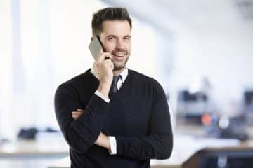 Portrait shot of handsome businessman standing in the office and using his mobile phone while making a call.