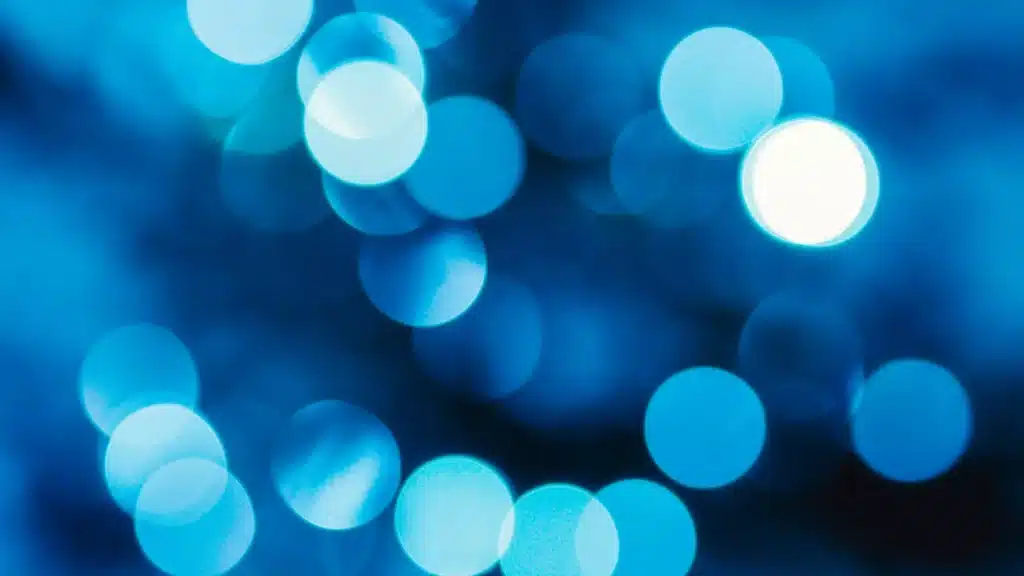 Blaue und weiße kreisförmige Lichtpunkte in einem verschwommenen, abstrakten Bokeh-Muster.