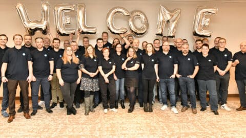 Eine Gruppe von Menschen in passenden Hemden steht vor einem großen WELCOME-Ballon.