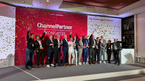 Eine Gruppe von Menschen auf der Bühne hält Trophäen, während goldenes Konfetti auf eine Veranstaltung fällt.