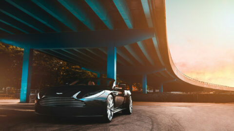 Ein schwarzer Sportwagen mit Cabrio ist bei Sonnenuntergang unter einer großen blauen Überführung geparkt.