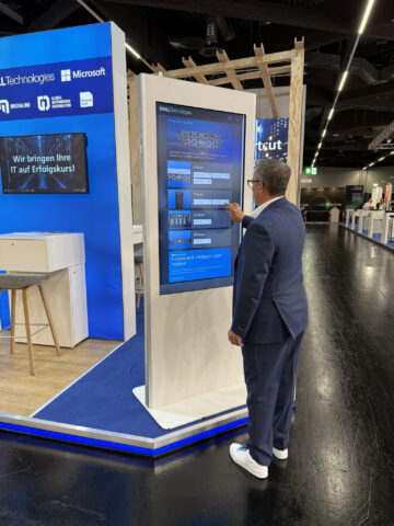 Ein Mann im Anzug benutzt einen großen Touchscreen auf einem Technologiestand.