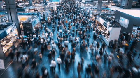 Eine große Menschenmenge, die durch eine belebte Kongresshalle oder eine Fachmesse läuft.