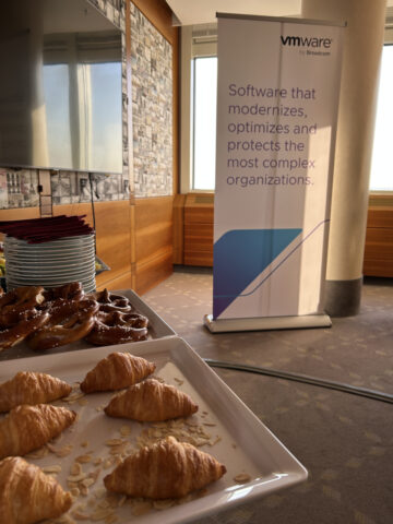 Teller mit Gebäck auf einem Tisch neben einem VMware-Banner in einem sonnendurchfluteten Konferenzraum.