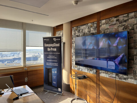 Konferenzraum mit einem Präsentationsbildschirm, einem Banner, einem Tisch und einem Fenster mit Blick auf einen Flughafen.