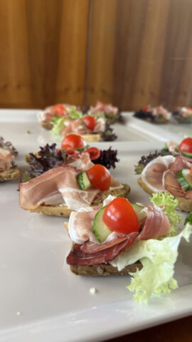 Offene Sandwiches mit Prosciutto, Salat, Gurke und Kirschtomaten auf einem weißen Tablett.