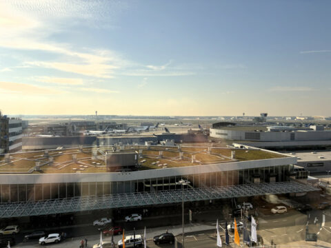 Blick auf ein Flughafenterminal mit geparkten Flugzeugen und Autos unter einem klaren Himmel.