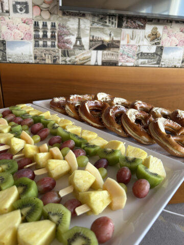 Tablett mit Obstspießen und Brezeln auf einem Tisch mit einer Pariser Tapete als Hintergrund.